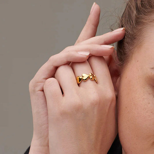 A close-up of a person's hand showcasing a gold ring with heart motifs on the finger.