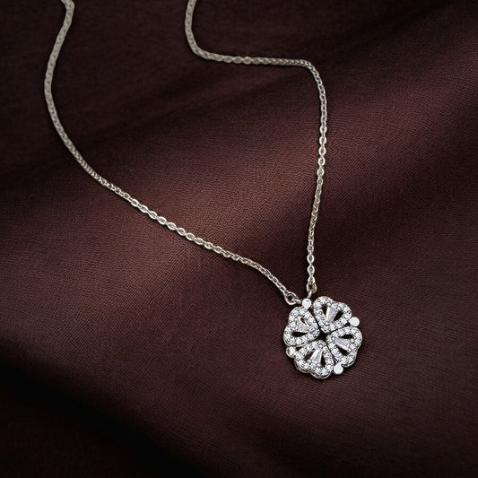 A silver necklace with an open heart chain pendant, featuring a clear crystal or stone in the center, displayed on a dark fabric background.