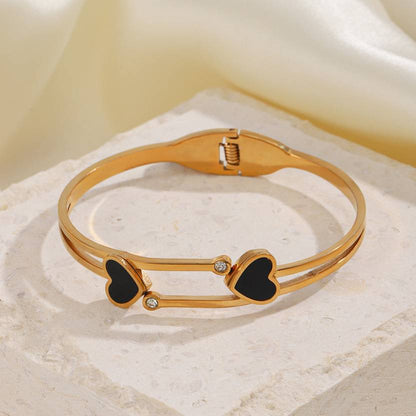 A 18k heart shape gold bangle bracelet with black heart accents and small white gemstones.