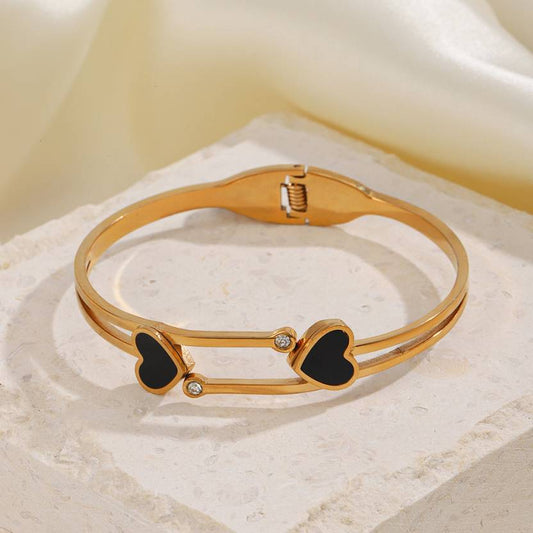 A 18k heart shape gold bangle bracelet with black heart accents and small white gemstones.