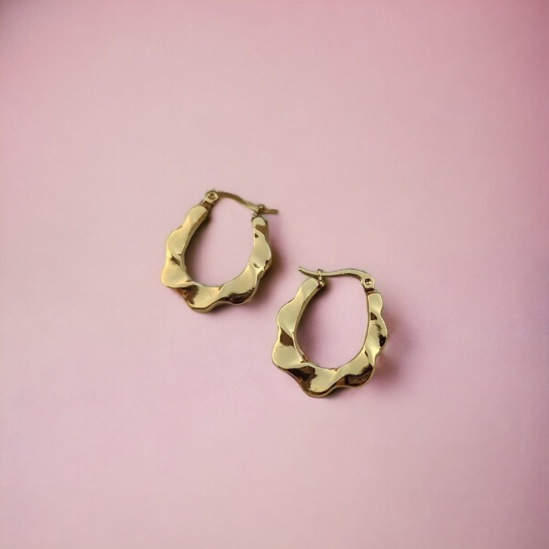 A pair of 18kt gold bamboo hoop earrings displayed on a pink background.