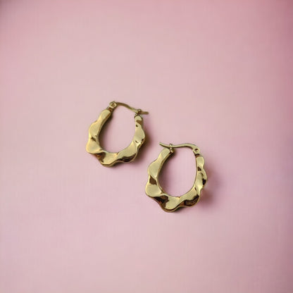 A pair of 18kt gold bamboo hoop earrings displayed on a pink background.