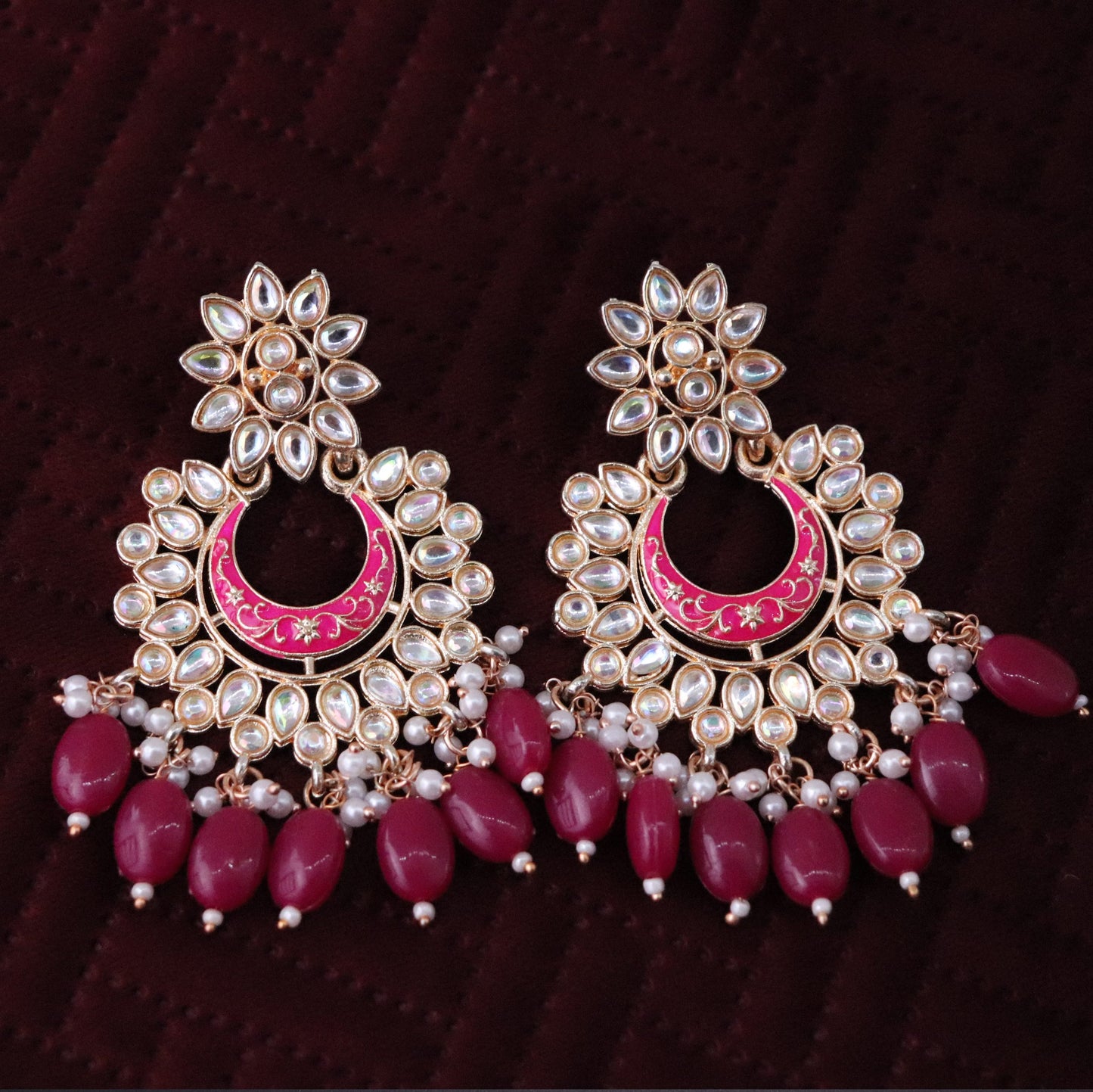 A pair of magenta colored chandbali earrings with floral patterns and pearl embellishments.