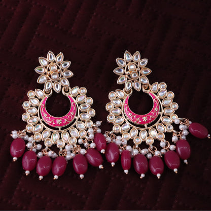 A pair of magenta colored chandbali earrings with floral patterns and pearl embellishments.