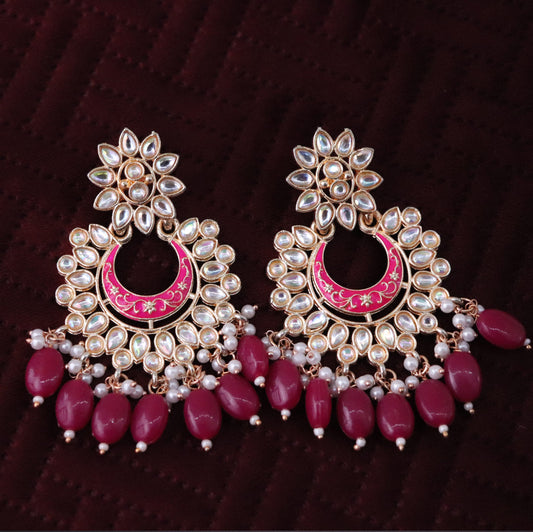 A pair of magenta colored chandbali earrings with floral patterns and pearl embellishments.