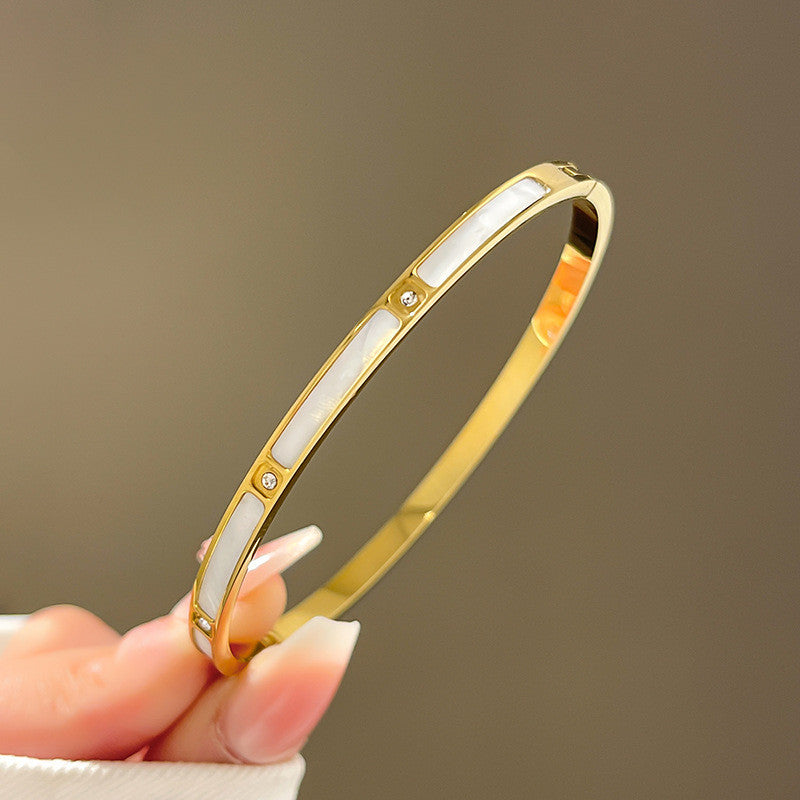 A 18K gold bangle bracelet with white inlay and small diamond-like embellishments held between fingers.