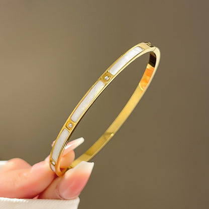 A 18K gold bangle bracelet with white inlay and small diamond-like embellishments held between fingers.