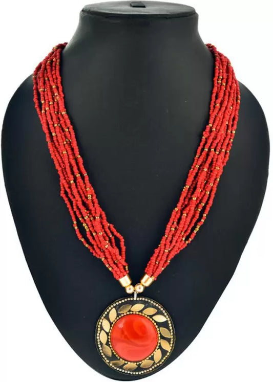 A red bead necklace with a golden sun-like pendant on a black mannequin bust.
