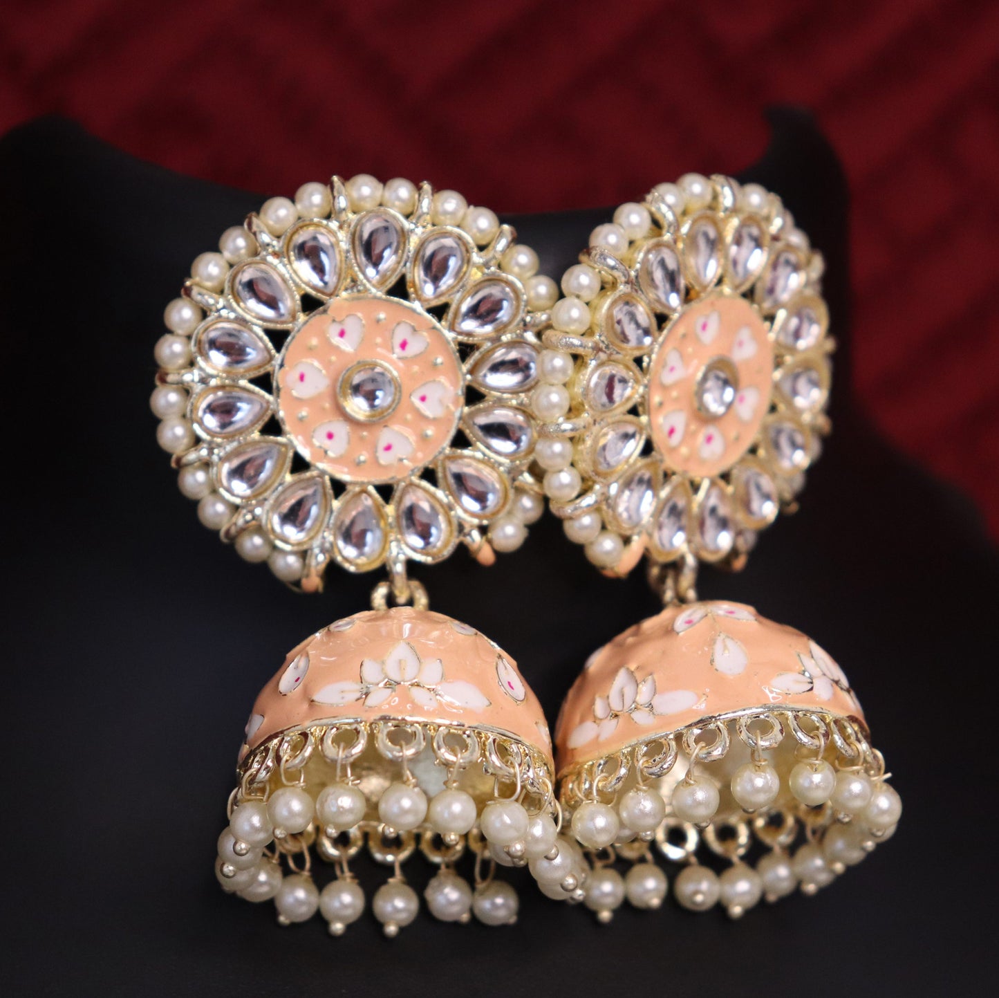 A pair of peach-colored pearl zinat blush jhumka earrings with intricate floral patterns and meenakari embellishments.