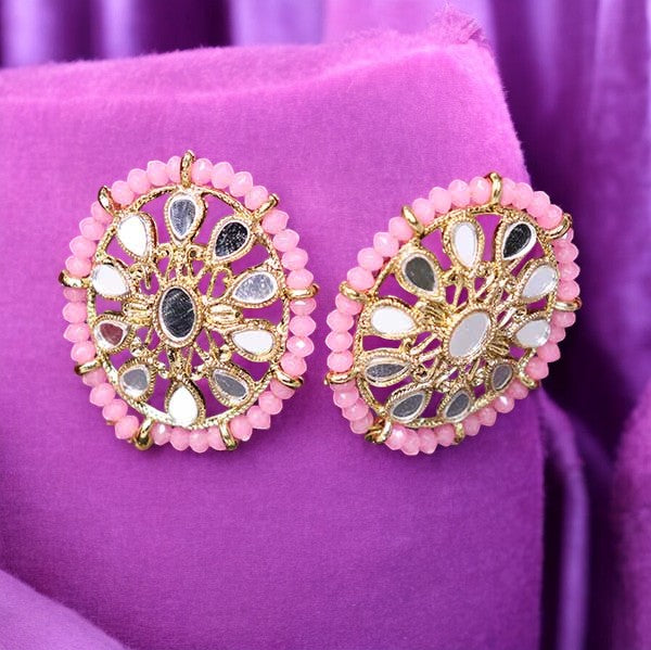 A pair of pink kundan earrings with gold accents, displayed on a purple fabric surface.