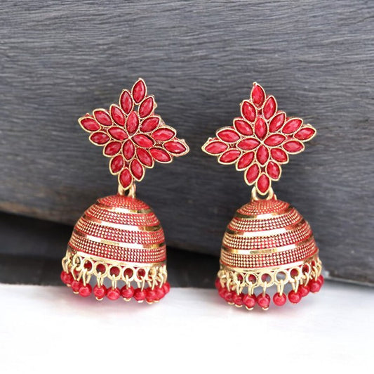 A pair of red floral jhumka bridal earrings with gold accents placed against a textured background.