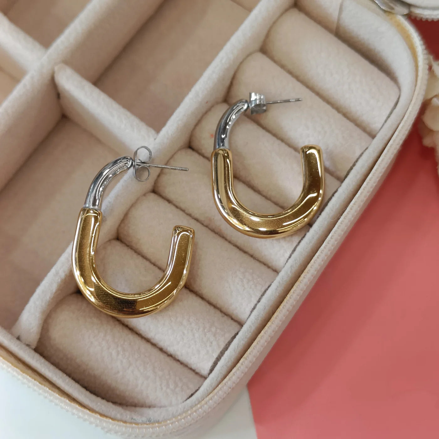 A pair of hoop earrings with a gold and silver design, placed in a beige cushioned jewelry box.