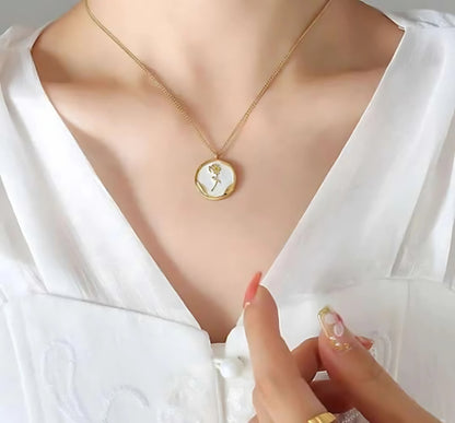 A person wearing a white shirt showcasing a gold chain pendant necklace with a heart-shaped locket on the chest.